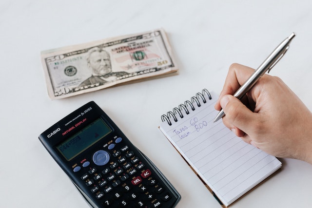 a calculator a stack of money and person making a budget